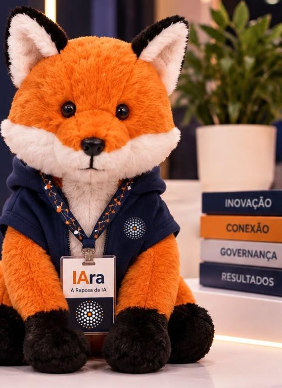 IA.RA, a Raposa da IA: raposa de pelúcia laranja com moletom azul-noite, logo IA no peito e crachá do evento